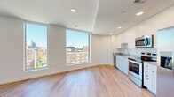 This thoughtfully designed single-floor residence showcases a clean, contemporary aesthetic defined by crisp white walls, light hardwood flooring, and an abundance of natural light throughout. Large, floor-to-ceiling windows are a defining architectural feature, appearing in virtually every room and framing sweeping elevated views of the surrounding urban skyline. The open living area is particularly striking, with multiple oversized windows spanning entire walls, flooding the space with sunlight and offering unobstructed cityscape panoramas.

The kitchen is well-equipped for modern living, featuring white shaker-style cabinetry extending to the ceiling, light granite countertops, and a full suite of stainless steel appliances including a side-by-side refrigerator, electric range, built-in microwave, and dishwasher. Recessed lighting adds a polished finish to the space.

The bedrooms maintain the home's bright, airy character, each benefiting from generous window placements with city views. One bedroom includes a dedicated walk-in closet with built-in shelving and a lighted interior. Hallways connect the rooms cleanly, reinforcing the space's efficient and modern layout. The overall ambiance is fresh, minimalist, and urban.