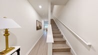 This two-story home offers a thoughtfully designed layout spread across two floors, combining functional living spaces with a clean, modern aesthetic. The main level features an open-concept kitchen, dining, and living area anchored by light hardwood flooring and a bright, neutral color palette. The kitchen is equipped with stainless steel appliances, white cabinetry, and a granite countertop island, while the dining area provides an inviting space for gatherings. The living room benefits from large windows that allow natural light to fill the room. A staircase with warm wood treads and a white railing connects the two floors, with a hallway adorned with framed wall art leading toward the common areas. The upper floor hosts three bedrooms, including a generously sized primary bedroom with a walk-in closet featuring built-in wire shelving. Two dedicated office spaces provide flexible areas for work or study. Four bathrooms are distributed throughout the home to accommodate both residents and guests. Recessed lighting, white trim, and consistent hardwood-style flooring unify the interior with a cohesive, contemporary feel, creating a comfortable and practical living environment.
