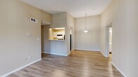 This single-floor residence offers a practical and well-organized layout across four bedrooms, two bathrooms, a living room, dining room, and kitchen. The open-plan living and dining area is immediately notable for its vaulted ceiling, which lends a sense of spaciousness beyond the unit's compact footprint. Light hardwood-style flooring extends throughout these shared spaces, complemented by neutral beige walls that create a clean, cohesive aesthetic. A pendant light fixture anchors the dining area, which connects directly to the kitchen via a pass-through opening, promoting an open and communicative flow between spaces.

The kitchen is galley-style, featuring white cabinetry, a double-basin stainless steel sink, light countertops, a dishwasher, and a full-size refrigerator. A closet accessible from the kitchen provides additional storage.

The bedrooms present a quieter, more private atmosphere. The primary bedroom offers a comfortable footprint with hardwood-style flooring and a window admitting natural light, while additional bedrooms feature soft carpeting and textured ceilings. The two bathrooms include tub-shower combinations with white tile surrounds and chrome fixtures, maintaining a consistent, functional design throughout the home.