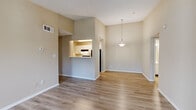 This single-floor residence offers a practical and well-organized layout across four bedrooms, two bathrooms, a living room, dining room, and kitchen. The open-plan living and dining area is immediately notable for its vaulted ceiling, which lends a sense of spaciousness beyond the unit's compact footprint. Light hardwood-style flooring extends throughout these shared spaces, complemented by neutral beige walls that create a clean, cohesive aesthetic. A pendant light fixture anchors the dining area, which connects directly to the kitchen via a pass-through opening, promoting an open and communicative flow between spaces.

The kitchen is galley-style, featuring white cabinetry, a double-basin stainless steel sink, light countertops, a dishwasher, and a full-size refrigerator. A closet accessible from the kitchen provides additional storage.

The bedrooms present a quieter, more private atmosphere. The primary bedroom offers a comfortable footprint with hardwood-style flooring and a window admitting natural light, while additional bedrooms feature soft carpeting and textured ceilings. The two bathrooms include tub-shower combinations with white tile surrounds and chrome fixtures, maintaining a consistent, functional design throughout the home.