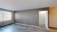 This 1-bedroom, 2-bathroom unit is laid out on a single floor, offering a practical and efficient use of space. The open living room is finished with wood-tone laminate flooring and neutral gray accent walls with clean white trim, creating a simple, modern aesthetic. A baseboard heating system runs along the perimeter, and the room connects directly to the rest of the unit via a hallway.

The galley-style kitchen is fitted with warm oak cabinetry on both walls, providing ample upper and lower storage. It includes a double-basin sink, a dishwasher, a white electric range with overhead ventilation, and a full-size refrigerator, all set above light laminate flooring.

The bedroom is a comfortable size, featuring the same laminate flooring found throughout, soft gray walls, a ceiling fan, and a large window with vertical blinds that allows for natural light and outside views. A wall-mounted air conditioning unit is also present.

The two bathrooms offer functional layouts. One features a full soaking tub with white square tile surround and chrome fixtures. The second bathroom includes a tub/shower combo, a wood-toned vanity with a light countertop, and a toilet, all finished in neutral tones. A hallway connects the rooms, completing this straightforward and well-organized unit.