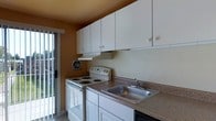 Located at 333 North Avenue in Secane, Pennsylvania, this single-floor space offers a practical and well-organized layout designed for comfortable everyday living. The kitchen is a central feature of the unit, showcasing an abundance of white upper cabinetry that provides generous storage space. The countertops are finished in a neutral brown laminate, complementing the stainless steel double-basin sink. A white electric coil range and oven anchor the cooking area, accompanied by a ventilation hood for efficient air circulation. A wall-mounted exhaust fan adds additional ventilation to the space. The warm, earthy tones of the walls lend a cozy ambiance to the kitchen. Natural light filters in through a sliding glass door adjacent to the kitchen, offering a view of the surrounding outdoor area and creating a bright, airy feel. The tile flooring throughout contributes to the clean, easy-to-maintain aesthetic of the space. The overall design is straightforward and functional, making efficient use of the available space while maintaining a comfortable and livable atmosphere throughout the single-level layout.