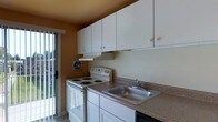 Located at 333 North Avenue in Secane, Pennsylvania, this single-floor space offers a practical and well-organized layout designed for comfortable everyday living. The kitchen is a central feature of the unit, showcasing an abundance of white upper cabinetry that provides generous storage space. The countertops are finished in a neutral brown laminate, complementing the stainless steel double-basin sink. A white electric coil range and oven anchor the cooking area, accompanied by a ventilation hood for efficient air circulation. A wall-mounted exhaust fan adds additional ventilation to the space. The warm, earthy tones of the walls lend a cozy ambiance to the kitchen. Natural light filters in through a sliding glass door adjacent to the kitchen, offering a view of the surrounding outdoor area and creating a bright, airy feel. The tile flooring throughout contributes to the clean, easy-to-maintain aesthetic of the space. The overall design is straightforward and functional, making efficient use of the available space while maintaining a comfortable and livable atmosphere throughout the single-level layout.