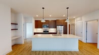This single-floor unit showcases a contemporary design with a thoughtful layout and quality finishes throughout. The open-concept kitchen serves as the heart of the space, featuring rich dark wood cabinetry, a white quartz waterfall island with an undermount sink, stainless steel appliances including a refrigerator, range, and built-in microwave, and a classic subway tile backsplash. Pendant lighting above the island adds a refined touch, while recessed lighting illuminates the space evenly. The kitchen flows naturally into adjacent living areas, which feature warm luxury vinyl plank flooring and built-in shelving.

Bedrooms are finished with plush carpeting and large black-framed windows that bring in generous natural light and exterior views. One room features sliding glass doors opening directly onto a private balcony with metal railings and stone column accents. A walk-in closet with wire shelving systems provides ample storage.

The bathroom includes a grey vanity with a clean white countertop, a mirror, and grab bars, all set on matching LVP flooring. A dedicated laundry area houses a stacked washer and dryer unit alongside additional wire shelving, offering practical convenience within the unit.