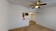 This single-floor unit offers a functional and straightforward layout designed for comfortable everyday living. The living area is open and airy, featuring neutral white walls, plush wall-to-wall carpeting, and a ceiling fan with a light fixture overhead. A pass-through counter connects the living space to the kitchen, maintaining an open feel while defining each zone. The entry area transitions seamlessly from hard flooring into the carpeted living space, with a window allowing natural light to filter in.

The galley-style kitchen is efficiently designed, featuring dark espresso-toned cabinetry on both sides, light countertops, a stainless steel sink, and black appliances including an electric range and refrigerator. Wood-look flooring runs throughout the kitchen, and overhead lighting keeps the space well-lit.

The bedrooms are carpeted and bright, each equipped with ceiling fans and windows fitted with horizontal blinds that provide natural light and privacy. The rooms offer clean, neutral walls and ample space for furnishings.

The bathroom includes a full tub and shower combination with white tile surround, a toilet, and a vanity with a countertop. Overall, the unit presents a clean, no-frills interior with practical finishes throughout.