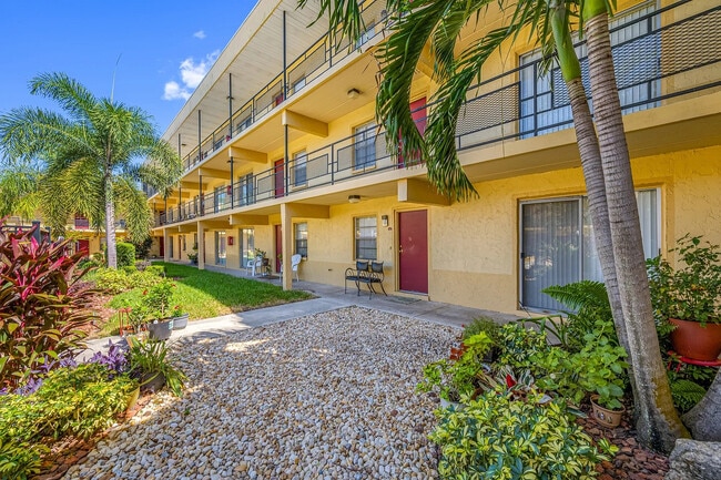 Charming two-story apartment community with vibrant garden landscaping and palm trees, set under a clear blue sky. - Parkview Apartments