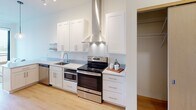 Located at 110 N First St in the North Loop neighborhood of Minneapolis, MN, this thoughtfully designed single-floor residence offers a clean, contemporary aesthetic throughout. The galley-style kitchen is a standout feature, outfitted with crisp white shaker cabinetry, sleek quartz countertops, stainless steel appliances including a range with a bold stainless range hood, a dishwasher, and a built-in microwave. A globe pendant light and track lighting illuminate the space, while open floating shelves add both function and style. The kitchen flows naturally toward the living area, which benefits from floor-to-ceiling windows that invite abundant natural light and provide access to an outdoor balcony with open views of the surrounding cityscape. The bedroom continues the bright, modern palette, featuring a large sliding wood-panel closet door, a floor-to-ceiling window framing elevated views of the Minneapolis skyline, and warm light wood flooring. The bathroom offers a clean, spa-like feel with a dual-sink vanity topped with white quartz, ample cabinetry, and an adjacent walk-in closet with built-in wire shelving. Light wood flooring runs consistently throughout the living spaces, tying the residence together with warmth and cohesion.