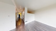 Located in Seattle's Dexter Hayes building, this well-designed one-bedroom, one-bathroom residence offers a smart, functional layout across a single floor. The open living area is bright and clean, featuring wide-plank hardwood-style flooring and large windows that invite natural light and provide views of the surrounding neighborhood. The galley-style kitchen runs along a corridor and is outfitted with stainless steel appliances — including a refrigerator, range, and over-the-range microwave — complemented by light wood cabinetry, white upper cabinets, white quartz-style countertops, and a classic subway tile backsplash. The kitchen opens toward the living space, creating a natural flow throughout the unit. A hallway connects the main living area to the private bedroom, which features its own large window offering additional natural light and street views. The bathroom is clean and functional, featuring a combination tub and shower with a curved curtain rod, a vanity with wood-toned cabinetry, and hardwood-style flooring. A dedicated closet provides practical storage. The unit's modern, minimalist design is consistent throughout, with crisp white walls, neutral tones, and quality finishes that create a cohesive and comfortable living environment.