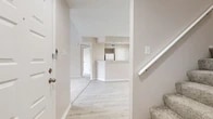Located at 3813 Brandywine Dr in Bedford, TX, this two-story home offers 2 bedrooms and 2 bathrooms thoughtfully distributed across two equally sized floors. The main level welcomes you with light wood-look flooring that flows through the entry and into the combined kitchen and living area. The kitchen is well-appointed with white cabinetry, granite-style countertops, a breakfast bar, and white appliances including a range with overhead microwave. The living room is a standout space, featuring soaring vaulted ceilings that draw the eye upward, a classic brick-hearth fireplace, and large windows that fill the room with natural light. An open staircase with a white balustrade connects the two levels. Upstairs, plush carpet runs throughout the bedrooms and hallway. The primary bedroom is a comfortable retreat with a closet and natural light. Both bathrooms are clean and functional, featuring tiled tub-shower combinations and wood-look flooring. A second carpeted bedroom provides additional flexibility. Neutral warm-beige tones and textured ceilings are consistent throughout, lending the home a cohesive and move-in-ready aesthetic.