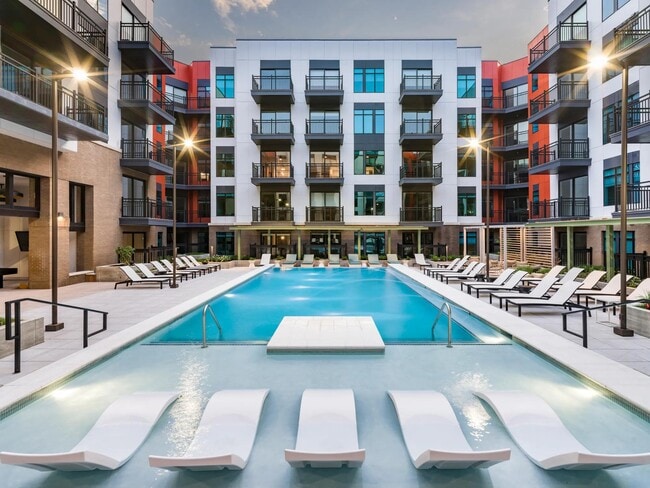 Resort-style pool courtyard with in-water loungers, sundeck seating, and private balconies surrounding the space. - Modera SoBro Apartments