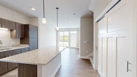 Located at 3375 Foundry Way in Wauwatosa, Wisconsin, this two-story home offers four bedrooms and two bathrooms across two well-proportioned floors. The main level sets a contemporary tone with light hardwood-style flooring, recessed lighting, and an open-concept layout that connects the kitchen and living areas seamlessly. The kitchen is a standout feature, boasting rich dark-toned cabinetry, stainless steel appliances including a refrigerator, range, and over-the-range microwave, granite countertops, and a generous island with pendant lighting overhead. Large windows at the front of the living area invite abundant natural light and provide views of the surrounding greenery. A staircase with built-in steps leads to the upper level, where four carpeted bedrooms offer comfortable, quiet retreats. The primary bedroom includes direct outdoor access through expansive windows and a sliding door. Bedrooms are serviced by closets featuring wire shelving systems, including a spacious walk-in closet. The bathrooms are finished with warm wood-toned vanities, granite countertops, and hardwood-style flooring. A dedicated laundry area with a stacked washer and dryer adds everyday convenience. Neutral tones throughout create a clean, modern ambiance.