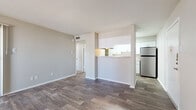 This single-floor residence features a cohesive, modern design highlighted by wood-style plank flooring that extends throughout the main living areas. The open living room offers generous wall space, neutral gray tones, and a pass-through window that connects to the kitchen, enhancing the sense of openness between spaces. A doorway from the living area leads further into the unit, providing a practical and straightforward layout.

The galley-style kitchen is well-appointed with white cabinetry featuring brushed nickel hardware, light granite-style countertops, a stainless steel refrigerator, an electric range with overhead ventilation, a dishwasher, and a stainless steel sink. Ample upper and lower cabinet storage makes this kitchen highly functional.

The bedroom is finished with plush carpeting and includes a ceiling fan with a light fixture. A window fitted with blinds allows natural light to fill the room. An additional room with wood-style flooring and a window provides flexible use as a secondary bedroom or office.

The bathroom is finished with wood-style flooring, white cabinetry, granite-style countertops, a framed mirror, and a full tub-shower combination, maintaining the clean, consistent aesthetic found throughout the space.