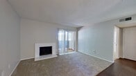 This single-floor residence offers a practical and comfortable layout across two bedrooms and two bathrooms. The living room serves as the heart of the home, featuring a white tile-surround fireplace and sliding glass doors that open to a private balcony, allowing natural light to fill the carpeted space. The entryway transitions from hardwood-style flooring into the living area, with a ceiling fan overhead adding to the room's functionality.

The galley-style kitchen is efficiently designed with white cabinetry, white countertops, and matching white appliances including a refrigerator, dishwasher, and range. Hardwood-style flooring runs throughout the kitchen, adding a clean contrast to the bright cabinetry.

Both bedrooms are carpeted and feature ceiling fans with integrated lighting. The primary bedroom includes access to a dedicated closet. The second bedroom is comfortably sized with a natural light source from a window.

The two bathrooms are functional and straightforward in design. One bathroom features a tiled tub-shower combination with floor-to-ceiling tile surround and chrome fixtures. The other includes a vanity with a white countertop, under-sink cabinetry, and a large mirror. Textured ceilings are consistent throughout the residence, contributing to a cohesive aesthetic.