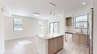 This well-designed 2-bedroom, 2-bathroom residence in Hialeah, FL offers a clean, modern aesthetic throughout its single-floor layout. The open-concept kitchen and living area serves as the heart of the home, featuring a central island with a crisp white quartz countertop and warm wood cabinetry that extends to the full kitchen. Stainless steel appliances, including a refrigerator, range, and microwave, complement the contemporary design, while pendant lighting above the island adds a refined touch. A sliding glass door floods the living area with natural light and provides outdoor access. Light wood-tone flooring flows consistently throughout the space, enhancing the bright, airy atmosphere created by the neutral cream-toned walls. Both bedrooms are generously proportioned, with large windows offering views of surrounding greenery, including glimpses of palm trees characteristic of the South Florida setting. The primary bedroom includes access to a dedicated closet. The bathrooms feature modern wood-grain vanities with white countertops and illuminated mirrors. A standout functional feature is the in-unit laundry area with a full-size washer and dryer. A hallway with a walk-in closet provides additional storage, completing this thoughtfully organized home.
