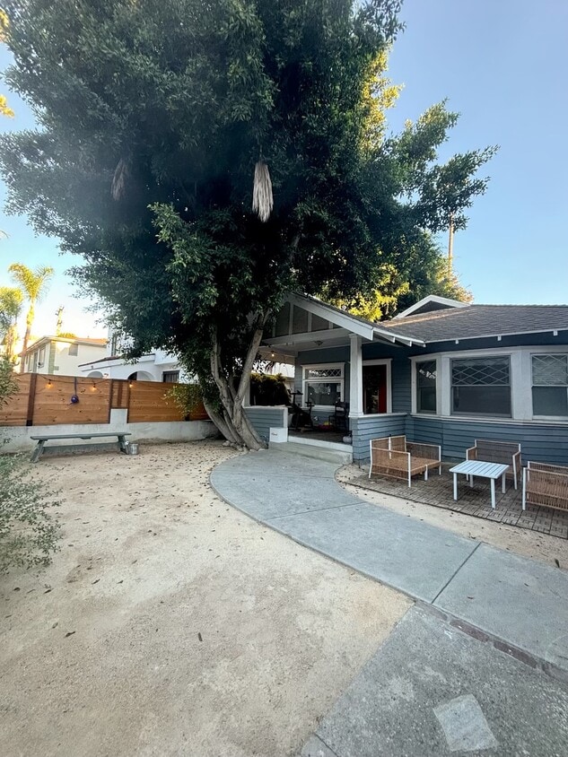 Spacious private front yard with mature tree and seating area, perfect for relaxing outdoors. - 6000 Carlton Way