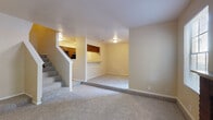 This two-story residence at 16550 Henderson Pass in San Antonio, Texas, offers a functional and comfortable layout spread across two floors. The main level features a spacious living room anchored by a classic brick fireplace framed by multiple windows that invite natural light and views of the surrounding greenery. Soft carpet flooring flows throughout the living area, creating a warm and inviting atmosphere. Adjacent to the living room is a pass-through kitchen equipped with warm wood cabinetry, dark appliances including an electric range, over-the-range microwave, and refrigerator, along with durable wood-style flooring. A convenient half bathroom on the main level features rich dark wood cabinetry and a granite-style countertop. A carpeted staircase connects the main level to the upper floor, where the bedrooms are located. The primary bedroom includes direct access to an en-suite bathroom fitted with dark wood vanity cabinetry, a granite-style countertop, and a tub-shower combination. A second full bathroom mirrors similar finishes with neutral tones and clean fixtures. Additional carpeted bedrooms on the upper floor offer versatile space for various needs. Throughout the residence, neutral wall tones and consistent finishes create a cohesive and understated aesthetic.