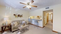 Located at 405 Garden Ln in Huntington, West Virginia, this efficiently designed one-bedroom, one-bathroom unit offers a well-organized single-floor layout. The living room serves as the heart of the space, featuring soft carpeted flooring, warm neutral walls, and a ceiling fan with integrated lighting. A front-facing window allows natural light to fill the room, creating a bright and welcoming atmosphere. The living area connects seamlessly to the kitchen via a convenient pass-through counter with bar seating, making the space feel open and functional. The kitchen is equipped with wood-toned cabinetry and standard appliances, providing all essential amenities in a compact footprint. A hallway connects the main living area to the private bedroom, which is carpeted and benefits from a window that brings in additional natural light. The bedroom comfortably accommodates a full-size bed and supporting furniture such as a dresser. The textured ceiling detail is consistent throughout the unit, adding a subtle architectural element. The bathroom features a clean, full-sized tub and shower combination with a curtain enclosure. Overall, the unit offers a practical and cozy living environment well-suited for individuals or couples.