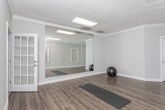 Located at 10300 Springs Ln in Peachtree Corners, GA, this single-floor space is thoughtfully designed for fitness and recreation. The layout includes multiple open rooms finished with durable wood-look luxury vinyl flooring throughout, neutral gray walls, and clean white baseboards and crown molding that lend a polished, cohesive aesthetic.

The centerpiece of the space is a dedicated fitness studio featuring full wall-to-wall floor-to-ceiling mirrors, ideal for monitoring form during workouts. Overhead flush-panel lighting ensures consistent, bright illumination, while a ceiling-mounted HVAC vent maintains a comfortable environment during exercise. A window fitted with white horizontal blinds allows for natural light.

Adjacent rooms provide additional flexible space, each maintaining the same consistent flooring and neutral color palette. One room opens directly into a recreation area where a billiards table is visible, highlighting the space's potential for leisure activities. The rooms are well-lit with both overhead lighting and natural light filtered through blinds-equipped windows.

Throughout the space, clean lines, minimal ornamentation, and an open floor plan create a versatile environment well-suited for fitness training, yoga, recreation, or a variety of other uses. The overall ambiance is modern, functional, and move-in ready.