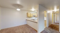 This two-bedroom, two-bathroom unit in Spokane Valley, WA offers a well-organized single-floor layout designed for comfortable everyday living. The open-concept living area features warm neutral-toned carpet throughout and flows seamlessly into the kitchen via a peninsula counter with a built-in sink, providing an ideal space for casual dining or meal prep. The kitchen is equipped with light oak cabinetry on both sides, a white electric range, refrigerator, and ample counter space, making it both functional and efficient. A sliding glass door in the carpeted living room fills the space with natural light and provides direct access to a private patio with outdoor views. Both bedrooms are carpeted and feature neutral walls; the primary bedroom offers a generously sized footprint, while the second bedroom includes a window with natural light. The two bathrooms are finished with tile flooring, wood-toned vanities, and standard fixtures — one includes a walk-in shower, and the other a full soaking tub with shower. A dedicated in-unit laundry area with washer and dryer hookups adds everyday convenience, complemented by a utility room, hallway, and closet for additional storage throughout the home.
