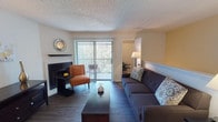 This Raintree apartment offers a well-organized single-floor layout across several distinct living areas. The living room serves as the heart of the home, featuring a striking black fireplace with a sleek mantel, wood-style flooring, and a sliding glass door that opens to a private balcony with outdoor seating and tree-lined views, filling the space with natural light. Adjacent to the living room, the dedicated dining area is defined by a pendant light overhead, chair rail molding, and the same wood-style flooring, creating a clean and inviting setting for meals. The galley-style kitchen is efficiently designed with dark cabinetry, granite-look countertops, and black appliances, including a full-size refrigerator, with a separate pantry or utility room nearby. The unit includes two bedrooms, each carpeted and featuring windows that allow natural light, offering comfortable and private retreats. Both bathrooms are similarly appointed, featuring a tub-shower combination with white tile surround, dark cabinetry with overhead storage, and wood-style flooring, providing a cohesive and functional design throughout. The textured ceilings and neutral wall tones present throughout the unit tie the overall aesthetic together cohesively.