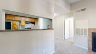 This single-floor residence offers a thoughtfully laid-out living space with a blend of comfort and functionality. The living area serves as the heart of the home, highlighted by a tile-surround fireplace with a classic glass door and soaring vaulted ceilings that amplify the sense of space. Built-in shelving flanks the fireplace, providing both display and storage opportunities. Plush, neutral-toned carpet runs throughout the living and bedroom areas, lending a warm and comfortable feel underfoot.

The kitchen is designed for efficiency, featuring a galley-style layout with warm honey-toned wood cabinetry, black appliances including a refrigerator and range, a built-in dishwasher, and a single-basin sink. Light wood-look flooring adds a clean, modern touch. A pass-through counter connects the kitchen to the living area, creating an open and social flow between spaces.

The bedroom is generously sized, bathed in natural light from a large window with exterior views, and finished with soft carpeting and a textured ceiling. The bathroom is well-appointed with warm wood cabinetry, a wide vanity with a round undermount sink, dual medicine cabinet mirrors, tile accents, and wood-look flooring for easy maintenance. Overall, the space presents a practical and inviting single-level layout.