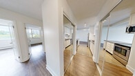 Located at 9502 Erickson Dr in Burnaby, BC, this well-appointed 3-bedroom, 1-bathroom unit offers a thoughtfully designed single-floor layout with modern updates throughout. The expansive living room is a standout feature, showcasing a full-width floor-to-ceiling window that frames lush treetop and cityscape views, flooding the space with natural light. Light-toned laminate hardwood flooring runs throughout the living and bedroom areas, complementing the clean, neutral palette of white walls and white baseboards. The renovated kitchen is both stylish and functional, featuring white cabinetry, subway tile backsplash, dark countertops, a breakfast bar peninsula, and stainless steel appliances including a refrigerator, stove, and built-in microwave. Tile flooring in the kitchen adds a practical contrast to the rest of the unit. The generously sized primary bedroom includes a mirrored sliding-door closet, while the additional bedrooms offer ample space with the same warm flooring. The bathroom is finished with white subway tile surrounding the bathtub, a large mirror, tile flooring, and a dark wood vanity with a light stone countertop. A private balcony with glass railings extends the living space outdoors, offering serene views of the surrounding greenery.