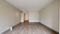 Located at 2280 N Tara Cir in Wichita, Kansas, this single-floor residence offers a clean, functional layout with a neutral and welcoming aesthetic throughout. The main living area is spacious and open, finished with light gray wood-look flooring that runs seamlessly throughout. Soft beige walls, white ceilings, and multiple HVAC vents contribute to a comfortable, well-maintained environment. Large vertical blinds along a wide sliding glass window wall flood the living space with natural light and provide views of mature trees outside, creating a bright and airy atmosphere.

A built-in kitchenette area features rich, dark wood cabinetry with under-cabinet storage, a compact refrigerator, and recessed lighting overhead — a practical and stylish touch within the open living space. The entry area transitions from tile flooring to the main living space, defined by a paneled front door that adds a classic architectural detail.

The bathroom is well-appointed with a warm wood vanity topped by a light stone-toned countertop, an under-mount sink, and a framed wood mirror. Tile flooring grounds the space, and a doorway leads to an adjacent closet or utility area. The overall ambiance of this residence is tidy, neutral, and move-in ready, suited for comfortable everyday living.