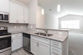 Located at 5301 Williamsburg Station Ln in Greensboro, North Carolina, this single-floor home offers a well-designed layout with a cohesive, neutral color palette and quality finishes throughout. The kitchen is a standout feature, showcasing white shaker-style cabinetry with crown molding, granite countertops, a classic subway tile backsplash, light hardwood-style flooring, and a full suite of stainless steel appliances including a refrigerator, electric range, and over-the-range microwave. Adjacent living areas are carpeted and finished with clean white baseboards, creating a warm and comfortable atmosphere. The primary bedroom is generously sized with vaulted ceilings, a ceiling fan, a large window that brings in ample natural light, and a walk-in closet with built-in shelving. Additional bedrooms are well-proportioned, each featuring carpet flooring, ceiling fans, and bright windows with blinds. The bathrooms are cleanly appointed with tiled flooring, soaking tub and shower combinations, and wall-mounted storage cabinets. Hallways and transitional spaces feature the same light hardwood-style flooring found in the kitchen, contributing to a consistent and polished interior design. The home presents a move-in ready environment with thoughtful details throughout.