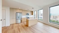 Located in the heart of downtown Raleigh at 320 West South Street, this modern 1-bedroom, 1-bathroom residence offers a thoughtfully designed open-concept layout with contemporary finishes throughout. Light wood flooring flows seamlessly across the entire unit, complementing the clean white walls and creating a bright, cohesive aesthetic.

The combined kitchen and living area serves as the centerpiece of the home. The kitchen is outfitted with flat-front light wood cabinetry, stainless steel appliances, a white tile backsplash, open shelving, and a centrally positioned island with a white countertop and an integrated sink — ideal for both cooking and casual dining. Floor-to-ceiling windows flood the space with natural light while framing sweeping elevated views of the Raleigh skyline and surrounding greenery.

The bedroom is a well-proportioned retreat featuring a large window with panoramic city views. Multiple closets provide generous storage throughout the unit. The bathroom features light wood vanity cabinetry, white tile flooring, and a clean, minimalist design. Additional conveniences include an in-unit laundry area, a pantry, a utility room, and a private balcony accessible from the living area, offering an outdoor space with elevated views of the cityscape.