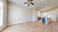 This two-story home offers a well-appointed layout across two floors, combining modern finishes with functional design. The main level features an open-concept kitchen and living area, finished with light-toned hardwood-style flooring that extends throughout. The kitchen is a standout, boasting stainless steel appliances including a French door refrigerator, electric range, microwave, and dishwasher. Two-tone cabinetry — white uppers paired with slate-blue lowers — frames the space, complemented by quartz countertops and a central island with built-in wine storage. Ceiling fans with recessed lighting are found throughout, adding both comfort and a clean aesthetic. A striking staircase with dark wood treads and white risers connects the floors, leading to the upper level. The generously sized primary bedroom features plush carpeting, a ceiling fan, natural light from a large window, and direct access to a private en-suite bathroom finished with large-format tile and a glass-enclosed walk-in shower with a built-in niche and bench. A dedicated laundry room with full-size washer and dryer, an additional bathroom, hallway, and closet round out the upper floor, making this home as practical as it is polished.