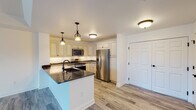 This single-floor residence offers a thoughtfully designed layout that balances functionality and modern aesthetics throughout. The kitchen serves as a central highlight, featuring cream-toned cabinetry with raised-panel detailing, dark granite countertops, and a full suite of stainless steel appliances including a gas range, over-the-range microwave, and French door refrigerator. A peninsula with an undermount sink and pendant lighting overhead adds both workspace and visual appeal, opening to the adjacent living area. Light wood-look flooring flows seamlessly through the kitchen and main living spaces, contributing to a bright, cohesive atmosphere.

The living area is generously proportioned, bathed in natural light through large sliding glass doors fitted with blinds. The bedrooms are finished with plush neutral carpeting and tray ceilings, with one room featuring a ceiling fan and a wide window overlooking the outdoors. The bathroom is finished with floor-to-ceiling marble-look tile, a tub-shower combination with a sliding glass door and oil-rubbed bronze fixtures, and a white vanity topped with dark granite. A dedicated laundry room provides full-size washer and dryer units, matching cabinetry, a utility sink, and utility connections, rounding out this well-equipped residence.