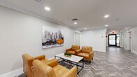 Located at 47 Legion Dr in Bergenfield, NJ, this single-level amenity space offers a thoughtfully designed environment spanning a generous footprint. The welcoming lobby lounge sets the tone upon entry, featuring herringbone-patterned luxury vinyl flooring, recessed lighting, and crown molding throughout. Tan leather armchairs arranged around a marble-top coffee table create an inviting seating area, complemented by a bold cityscape wall mural. A mounted flat-screen TV, dark wood credenza, and vending machine add functional convenience to the space, while glass entry doors allow natural light to filter in.

Wide, well-lit hallways connect the various areas seamlessly, maintaining a clean, modern aesthetic consistent throughout. The fully equipped fitness center is a standout feature, offering an extensive array of commercial-grade equipment including treadmills, stationary bikes, cable machines, free weights, and strength training stations. Rubber flooring, floor-to-ceiling mirrors, and industrial-style exposed ceiling details give the gym a dynamic, professional atmosphere. A water fountain and open shelving provide added utility.

The bathroom is finished with large-format marble-look wall tiles, herringbone floor tile, a floating wood-toned vanity with a white countertop, and a sleek black-framed mirror, reflecting the same refined design sensibility found throughout the entire space.