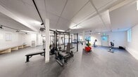 Located in Calgary, AB, this fitness centre spans a generous single floor, providing ample space for a full range of exercise activities. The facility features a clean, modern interior with white walls, a suspended tile ceiling with track lighting, and durable rubber flooring throughout — all designed to create a functional and motivating workout environment.

The strength training area is a standout feature, centered around a large multi-functional power rack system equipped with cable attachments, pull-up bars, and various weight stations. Colourful bumper plates and weight storage racks are conveniently positioned nearby, alongside adjustable benches and additional free weight equipment. A dedicated stretch and functional training zone includes resistance bands, a stability ball, a heavy bag, and adjustable incline benches, offering versatility for dynamic workouts.

The cardio section is well-appointed with multiple treadmills, an elliptical trainer, and upright and spin bikes, all positioned near windows that allow natural light to fill the space. A seating bench and water station provide a comfortable area for rest between sessions. The layout is thoughtfully organized to maximize floor space and ensure smooth circulation throughout the facility, making it a comprehensive fitness destination suitable for a wide range of training goals.