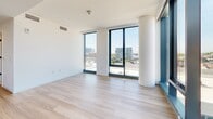 Located at 801 Orange Street in Wilmington, Delaware, this modern one-bedroom, one-bathroom unit offers a thoughtfully designed open layout with a bright, contemporary aesthetic throughout. Light hardwood flooring flows seamlessly across the entire space, complementing the clean white walls and modern finishes.

The open-plan living room and kitchen area is a standout feature, dominated by expansive floor-to-ceiling windows with sleek black frames that flood the space with natural light and frame sweeping elevated views of the Wilmington cityscape and surrounding neighborhoods. Architectural cylindrical columns add a refined structural detail to the living area.

The kitchen is outfitted with a full suite of stainless steel appliances, including a refrigerator, electric range, over-the-range microwave, and dishwasher. Gray flat-front cabinetry extends from floor to ceiling, providing generous storage, while the white countertops offer ample workspace.

The well-proportioned primary bedroom continues the floor-to-ceiling window theme, delivering abundant natural light and open city views, along with a dedicated closet. The bathroom features large-format earth-toned tile flooring, a soaking tub, and elegant marble-style tile surround, paired with a wood-toned vanity for a warm, upscale finish.