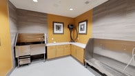 This single-level pet grooming room is thoughtfully designed to balance functionality with a welcoming atmosphere. The space is anchored by a vibrant amber-yellow accent wall that adds warmth and energy, contrasting elegantly with the neutral grey, wood-grain wall panels that line the surrounding walls and ceiling trim. Recessed lighting overhead ensures the room is well-lit, supporting precise grooming work throughout the day.

The room features an L-shaped run of light wood cabinetry with white countertops, providing ample storage and workspace for grooming supplies and tools. A wall-mounted professional grooming dryer is conveniently positioned along the accent wall for easy access. Two framed black-and-white photographs of pets are displayed above the counter, adding a charming, pet-friendly character to the space.

Stainless steel fixtures are prominent throughout, including what appears to be a grooming tub and a raised washing station, both designed for durability and easy sanitation. The seamless light-toned flooring is practical and easy to maintain. Overall, the space is clean, efficient, and professionally outfitted for high-quality pet grooming services.