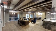 Located at 515 West Ave in Norwalk, Connecticut, this single-floor space offers a thoughtfully designed open layout that seamlessly blends comfort and rustic character. The most striking architectural feature is the ceiling, which is adorned with rich, dark exposed wooden beams that span the length of the room, adding warmth and a sense of history to the space. Wide-plank hardwood floors run throughout, complementing the earthy tones of the beams and creating a cohesive, inviting atmosphere.

The main living area is generously proportioned, centered around a classic leather Chesterfield sofa and accompanied by deep navy blue accent chairs with yellow throw pillows, lending a sophisticated yet approachable aesthetic. A large wooden coffee table anchors the seating arrangement, while ambient pendant lighting and recessed fixtures illuminate the space evenly.

The open floor plan flows naturally into a dedicated dining area, complete with a full dining table and chairs, positioned near a fireplace that adds an additional layer of warmth and elegance. Built-in shelving along one wall provides both functional storage and a curated display area. Natural light filters in through multiple windows and glass doors, keeping the interior bright and connected to the outdoors. A wall-mounted television adds a modern touch to this characterfully designed space.