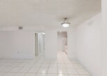 Located at 9000 SW 97th Ave in Miami, FL, this single-story unit offers a clean, bright interior defined by large-format white ceramic tile flooring that runs consistently throughout the entire space. The open living and dining area is generously proportioned, featuring a textured ceiling, flush-mount pendant lighting, and a neutral white palette that maximizes the sense of light and openness. Arched pass-throughs and interior doorways connect the living areas to the rest of the unit in a functional and cohesive layout.

The galley-style kitchen is well-appointed with white shaker cabinetry accented by brushed nickel hardware, granite countertops, a full suite of white appliances including an electric range, built-in microwave, and refrigerator, and track lighting overhead. The bedrooms are comfortably sized, with several offering natural light through roller shade–equipped windows and generous closet space, including double and bifold closet configurations. One bedroom provides views of surrounding greenery.

The bathroom features tile wainscoting, a tub and shower combination with sliding glass doors, a granite-topped vanity, and recessed lighting. A stacked washer and dryer unit is conveniently located near the main entrance, adding in-unit laundry functionality to this well-maintained Miami residence.