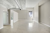 Located at 650 S Spring St in the heart of Downtown Los Angeles, this urban loft showcases the character-rich industrial aesthetic synonymous with the city's historic core. The single-floor layout offers an efficiently designed yet open living space with light-toned tile flooring throughout, creating a bright and cohesive atmosphere.

The main living area impresses with soaring ceilings that feature exposed concrete textures, structural beams, and visible ductwork — hallmarks of classic loft-style architecture. Large windows and a glass-paneled door open onto a private balcony with glass-railed fencing, bringing in an abundance of natural light and urban views of the surrounding Downtown streetscape.

The kitchen is well-appointed with rich dark wood cabinetry, stainless steel appliances including a refrigerator, range, and dishwasher, complemented by a stone-tiled backsplash and ample counter space. Frosted glass interior doors add a modern, translucent design element throughout.

The sleeping area connects to a dedicated walk-in closet, providing generous storage. The bathroom is a standout feature, finished with floor-to-ceiling mosaic glass tile in cool blue and gray tones surrounding a soaking tub and shower, paired with a dark vanity and warm stone countertop. This loft balances industrial character with modern finishes in a prime Downtown LA location.