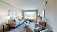 This single-floor residence offers a thoughtfully designed layout with a cohesive, neutral color palette and quality finishes throughout. The living room serves as the centerpiece of the home, featuring crown molding, large windows with sheer curtains and adjustable blinds that invite abundant natural light, and views of the surrounding exterior. The space accommodates a comfortable seating arrangement anchored by a plaid area rug, creating a warm and inviting atmosphere.

The kitchen is outfitted with rich dark cabinetry, granite countertops, a classic white subway tile backsplash, and a full suite of stainless steel appliances, including a range, microwave, and dishwasher. Wood-look flooring adds warmth to the space. Adjacent to the kitchen, the dining area features hardwood-style flooring and offers room for a full dining table, complemented by a decorative mirror accent on the wall.

Two bedrooms provide comfortable retreats, each with plush carpeting, natural light from windows with blinds and curtains, and ample space for bedroom furnishings. The two bathrooms are finished with wood-look tile flooring, dark vanity cabinetry with granite countertops, and shower-tub combinations, offering both style and functionality. Overall, the residence presents a clean, modern aesthetic with a warm and livable character.