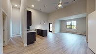 Located at 209 E Main St in Waunakee, Wisconsin, this thoughtfully designed single-floor residence showcases a contemporary open-concept layout with impressively tall ceilings throughout. The spacious kitchen is a standout feature, outfitted with rich dark cabinetry, stainless steel appliances including a refrigerator, range, and microwave, light quartz countertops, a tile backsplash, and a large peninsula with an undermount sink — all illuminated by stylish pendant lighting. The kitchen flows seamlessly into an expansive living area finished with light wood-look flooring and a ceiling fan overhead. A dedicated hallway leads to additional rooms, including a bedroom with plush carpeting, dramatic floor-to-ceiling grid-pane windows, and direct access to a private balcony offering views of the surrounding Waunakee streetscape. A second room with tall windows provides ample natural light. The unit includes two bathrooms: a full bath with a tub/shower combo and a second bath featuring a dark vanity with quartz countertop, a large mirror, tiled shower surround, and built-in open shelving. A conveniently located in-unit laundry closet houses a stacked washer and dryer. The neutral color palette and high ceilings create a bright, airy ambiance throughout.