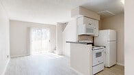 This two-story, one-bedroom, one-bathroom home is thoughtfully laid out across two evenly divided floors, offering a functional and efficient use of space. The main level features a bright living room with light wood-look luxury vinyl flooring and a sliding glass door dressed with vertical blinds, allowing natural light to pour in and providing access to the outdoors. Adjacent to the living room, a galley-style kitchen is equipped with white cabinetry, dark laminate countertops, white appliances including a range, built-in microwave, and refrigerator, all beneath a textured ceiling. The staircase, carpeted in a neutral tone, connects the two floors and features an angular wall opening that adds architectural interest to the transition between levels. Upstairs, the generously sized bedroom is carpeted for comfort and includes a dedicated closet with built-in shelving, as well as a textured ceiling consistent with the rest of the home. The full bathroom is located on the upper level and features a tiled shower/tub combination with a curtain, toilet, and vanity. Throughout the home, neutral warm tones, clean white trim, and consistent flooring materials create a cohesive and understated aesthetic.
