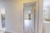 This thoughtfully laid-out one-bedroom, one-bathroom unit in Surrey, BC, offers a bright and clean living environment across a single floor. Light-toned hardwood flooring flows throughout the main living areas and bedroom, creating a cohesive and airy feel. The living room is a standout space, anchored by a white tile-surround wood-burning fireplace with a built-in hearth shelf, flanked by tall windows and a sliding glass door that opens to a private balcony overlooking lush greenery. Natural light fills the room, enhancing its open and welcoming ambiance. The galley-style kitchen is efficiently designed with white cabinetry, dark countertops, a tile backsplash, and full appliances including a refrigerator and electric range, with a separate pantry closet for added storage. Adjacent to the kitchen, a dining area features tile flooring and a large window with garden views. The bedroom is a comfortable, well-sized retreat with light hardwood floors, a window overlooking greenery, and a built-in closet with bifold doors. The bathroom is finished with warm beige wall and floor tiles, a white vanity with a marble-style countertop, and a large mirror. A hallway with additional closet storage connects the rooms efficiently throughout the unit.