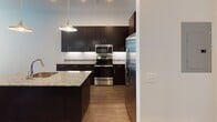 This single-floor space showcases a contemporary design with clean lines, an open-concept layout, and high-quality finishes throughout. The kitchen is a standout feature, equipped with dark espresso cabinetry, stainless steel appliances including a range, microwave, and refrigerator, complemented by granite countertops, a white subway tile backsplash, and stylish pendant lighting that adds a modern touch. A kitchen island with a sink provides additional workspace and functionality.

The open living area extends generously from the kitchen, featuring warm hardwood-style flooring that flows seamlessly throughout the space. The room benefits from elevated ceilings and recessed lighting, contributing to a bright and airy atmosphere. A built-in shelving unit and multiple doorways offer practical storage and easy access to adjoining rooms.

The bedroom is a calm and well-lit retreat, with large windows that invite natural light and a ceiling fan for year-round comfort. The hardwood-style flooring continues here, maintaining a cohesive aesthetic.

The bathroom is finished to a high standard, highlighted by a spacious glass-enclosed walk-in shower clad in large-format marble-look tile with elegant grey veining. Chrome fixtures and glass shelving complete the refined look. Overall, this space offers a polished, move-in-ready environment with thoughtful design details throughout.