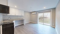 This efficiently designed single-floor studio offers a thoughtfully laid-out living space that maximizes every square foot. The open main area features light gray luxury vinyl plank flooring throughout, neutral gray walls, and recessed lighting that creates a bright, clean atmosphere. A wall-mounted mini-split HVAC unit ensures year-round comfort, while a large sliding glass door floods the space with natural light and provides direct access to an outdoor area with views of a landscaped yard.

The kitchen is outfitted with white shaker-style cabinetry, granite-look countertops, stainless steel appliances including a range and microwave, and a stainless steel refrigerator. The corner kitchen layout makes efficient use of the available space while maintaining an open feel throughout the main living area.

The entrance provides a welcoming transition into the unit, clearly defined from the main living and kitchen zones. The bathroom features a sleek, modern walk-in shower enclosed by a frameless glass panel, with large-format gray wall tiles and a white shower base, complemented by chrome fixtures and a corner caddy. Clean lines and a neutral palette tie all areas of the space together, resulting in a cohesive and contemporary interior.
