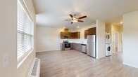 This well-designed 2-bedroom, 2-bathroom unit makes efficient use of its single-floor layout, offering a bright and modern living environment. The open-concept living and kitchen area is immediately distinguished by dramatically vaulted ceilings that amplify the sense of space, complemented by clerestory windows positioned high on the walls to draw in abundant natural light. A ceiling fan serves both the aesthetic and functional needs of the room, while a wall-mounted HVAC unit provides dedicated climate control. Multiple windows at standard height overlook the surrounding neighborhood, further enhancing the airy atmosphere.

The kitchen is outfitted with a full suite of stainless steel appliances—including a refrigerator, range, microwave, and dishwasher—paired with warm wood-toned cabinetry and clean white countertops arranged in an efficient L-shaped configuration.

Both bedrooms feature light wood-look flooring consistent with the rest of the unit, neutral walls, and windows that provide natural light and outdoor views. The primary bedroom benefits from an en-suite bathroom with a walk-in closet featuring built-in shelving and rod storage. A second bathroom includes a single vanity with wood cabinetry, a large mirror, and a shower-tub combination.