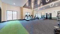 Located at 5720 Peachtree Pkwy in Peachtree Corners, GA, this single-story fitness facility offers a generously sized, thoughtfully designed workout environment spanning nearly 3,900 square feet. The space is organized into distinct functional zones, each equipped to support a wide range of training styles.

The main workout area features soaring ceilings adorned with a dramatic dark ceiling treatment accented by constellation-like detailing and suspended circular ring pendant lights, creating a visually striking atmosphere. Large windows along one wall provide views of surrounding wooded scenery, filling the space with natural light.

The cardio zone houses a row of treadmills, ellipticals, and stationary bikes positioned to take advantage of the outdoor views. The strength training area is lined with floor-to-ceiling mirrors that visually expand the space and includes cable machines, a power rack, Smith machine, free weights, and adjustable benches.

A dedicated functional training zone features artificial turf flooring, plyo boxes, a sled, and battle rope anchors, supported by wall-mounted televisions. Built-in cabinetry with open shelving provides organized equipment storage, while perforated wood accent panels add a refined design element. Steel-framed glass doors complete the polished, contemporary aesthetic throughout.