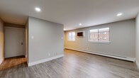 This single-floor unit offers a thoughtfully designed layout that balances open living areas with functional private spaces. Throughout, light-toned luxury vinyl plank flooring creates a cohesive, contemporary aesthetic, complemented by neutral gray walls and crisp white baseboards.

The main living area is generously proportioned, featuring recessed lighting and windows fitted with blinds that provide views of the surrounding brick building exterior. A wall-mounted air conditioning unit and baseboard heating ensure year-round comfort. The open floor plan connects the living space to a well-equipped kitchen, which features dark shaker-style cabinetry, a tiled backsplash, light countertops with an undermount sink, and a full suite of stainless steel appliances including a refrigerator and dishwasher.

The bedroom offers a comfortable and quiet retreat, equipped with a ceiling fan and light fixture, baseboard heating, and a dedicated walk-in closet with built-in shelving. A bathroom serves the unit with a dark-finished vanity, white countertop, mirrored medicine cabinet, and a separate shower area, all finished with darker tile flooring that adds contrast to the overall palette.