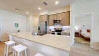 This single-floor residence is designed with a clean, contemporary aesthetic and an open-concept layout that connects the kitchen, dining, and living areas seamlessly. Light wood-tone flooring flows throughout, complementing the bright, neutral color palette that defines the space.

The kitchen is a standout feature, equipped with stainless steel appliances including a French door refrigerator, electric range, and built-in microwave. Warm wood cabinetry reaches to the ceiling, paired with a white subway tile backsplash. A generously sized quartz waterfall island with an integrated sink and bar seating serves as both a functional workspace and a casual dining hub. A dedicated dining nook with a round table sits adjacent to the kitchen alongside a stacked in-unit washer and dryer.

The living room benefits from floor-to-ceiling windows that allow abundant natural light and outdoor views, further enhanced by a ceiling fan overhead. Two bedrooms offer a calm retreat, each with light wood flooring and natural light from well-positioned windows. Two full bathrooms feature wood-toned vanities and light tile flooring, with the primary bath including a walk-in closet and separate shower.