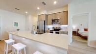 This single-floor residence is designed with a clean, contemporary aesthetic and an open-concept layout that connects the kitchen, dining, and living areas seamlessly. Light wood-tone flooring flows throughout, complementing the bright, neutral color palette that defines the space.

The kitchen is a standout feature, equipped with stainless steel appliances including a French door refrigerator, electric range, and built-in microwave. Warm wood cabinetry reaches to the ceiling, paired with a white subway tile backsplash. A generously sized quartz waterfall island with an integrated sink and bar seating serves as both a functional workspace and a casual dining hub. A dedicated dining nook with a round table sits adjacent to the kitchen alongside a stacked in-unit washer and dryer.

The living room benefits from floor-to-ceiling windows that allow abundant natural light and outdoor views, further enhanced by a ceiling fan overhead. Two bedrooms offer a calm retreat, each with light wood flooring and natural light from well-positioned windows. Two full bathrooms feature wood-toned vanities and light tile flooring, with the primary bath including a walk-in closet and separate shower.