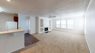 This single-story residence offers a thoughtfully arranged layout connecting the main living spaces in an open, functional design. The spacious living room serves as the focal point of the home, highlighted by a gas fireplace flanked by built-in shelving units, a ceiling fan, and a row of windows along one wall that invites natural light into the room. Neutral-toned carpet flows throughout the living and bedroom areas, complementing the light-colored walls and white trim.

The kitchen is well-equipped with rich, dark cherry wood cabinetry offering ample upper and lower storage, light countertops, a stainless steel sink, a dishwasher, and an electric range with an overhead ventilation hood. A breakfast bar peninsula separates the kitchen from an adjacent dining area, creating a seamless transition between spaces. The kitchen features tile flooring and recessed lighting alongside a ceiling-mounted fluorescent fixture. Crown molding accents the kitchen and dining area.

The bedrooms are carpeted and feature neutral walls, with at least one room including a double-door closet fitted with dual hanging rods and a shelf for organized storage. A window provides natural light to one of the bedrooms. The bathroom includes a tub/shower combination, a toilet, a single-sink vanity with dark wood cabinetry, a large mirror, and wood-look flooring, with a window providing ventilation above the tub.